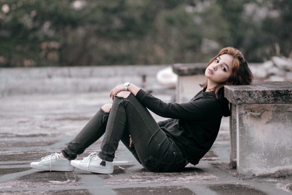 nastolatka ubrana na czarno siedzi na betonowej podłodze skate parku
