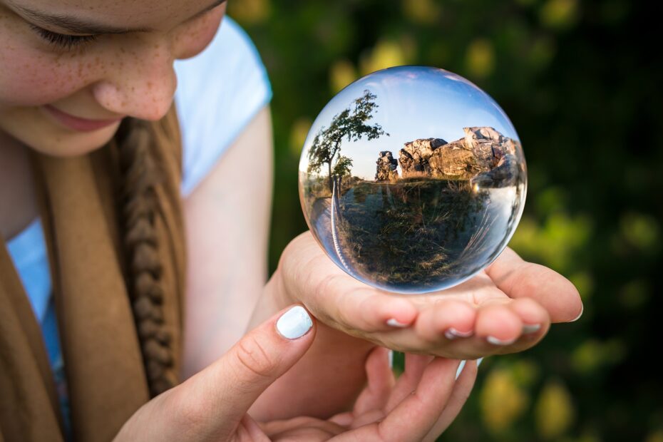 dziewczynka z warkoczami trzyma szklaną kulę w której widzi krajobraz