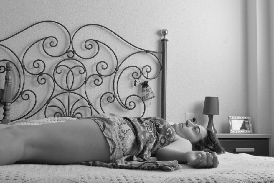 zdjęcie w odcieniach szarości. kobieta w sukience leży na łóżku na plecach patrząc w sufit.
