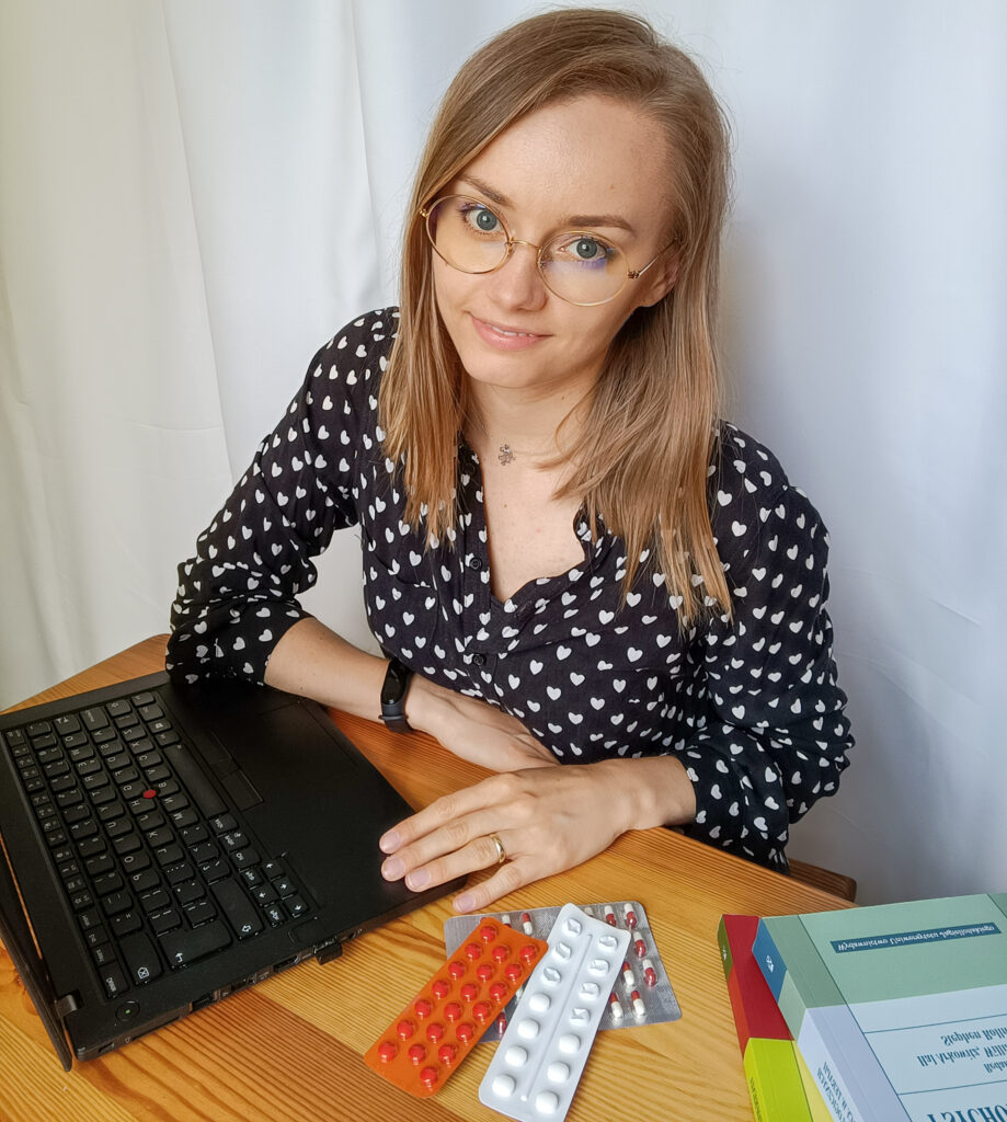 Julia Skibińska konsultacja psychologiczna online. Kobieta psycholog, drewniany stolik, laptop, blistry leków i książki psychologiczne.
