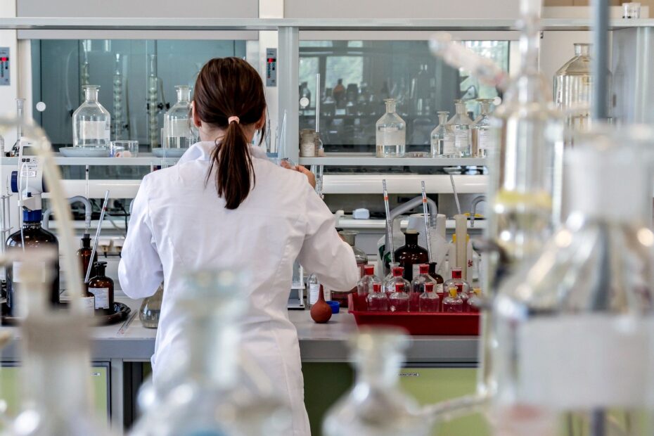 pracownica laboratorium wśród różnych naczyń i substancji laboratoryjnych. stoi tyłem w białym kitlu