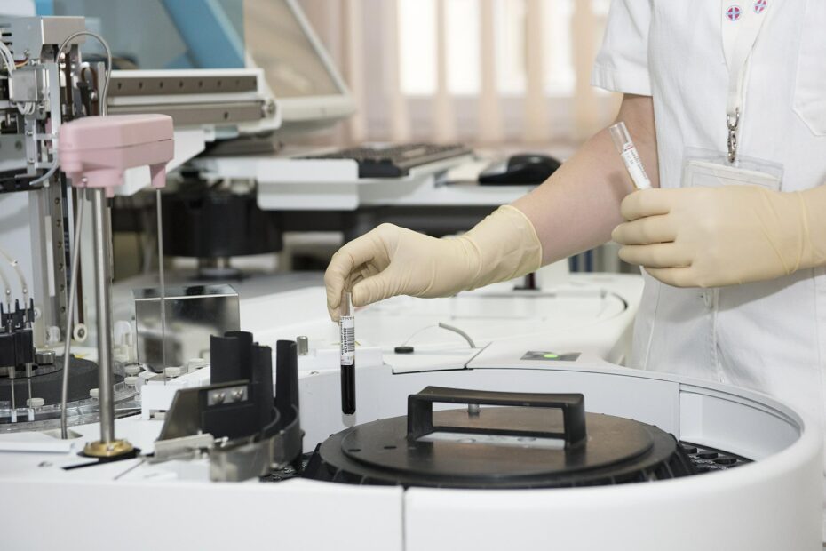 laboratorium. Naukowiec lub diagnosta sprawdza próbkę krwi. Widoczne są przeróżne przyrządy i maszyny laboratoryjne.